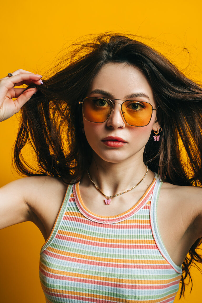 Portrait of attractive stylish woman in sunglasses with long brunette hair isolated on yellow background in studio.