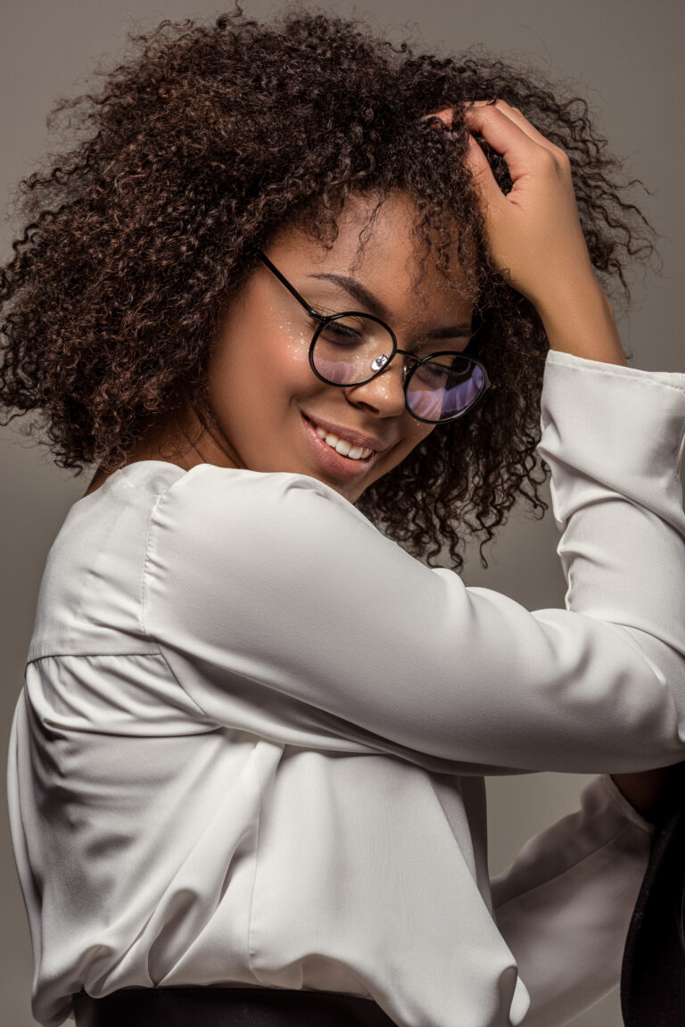 Young smiling african american woman in white shirt wearing glasses isolated on grey background